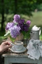 Breakfast in the garden: eclairs, cup of coffee, coffee pot, lilac flowers in a basket Royalty Free Stock Photo