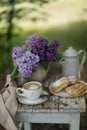 Breakfast in the garden: eclairs, cup of coffee, coffee pot, lilac flowers in a basket Royalty Free Stock Photo
