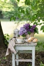 Breakfast in the garden: eclairs, cup of coffee, coffee pot, lilac flowers in a basket Royalty Free Stock Photo