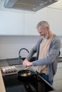 A gray-haired man cooking omlette in the kitchen