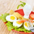 Breakfast with hard boiled eggs, sliced in halves, salad, tomatoes and cheese on the red plate Royalty Free Stock Photo