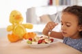 Breakfast with her best friend. a cute little girl eating fruit salad with her plush toy on the table. Royalty Free Stock Photo