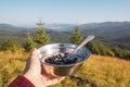 Breakfast in the hike, a bowl of porridge and berries in the female hand on the background of the morning mountain landscape