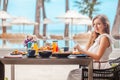 Breakfast in luxury hotel. Woman sitting in outdoor cafe, eating healthy food in hotel near swimming pool, sea and sun Royalty Free Stock Photo