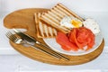 Breakfast menu: toasted bread, smoked salmon, poached eggs and cup of coffee on white windowsill