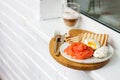 Breakfast menu: toasted bread, smoked salmon, poached eggs and cup of coffee on white windowsill