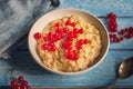 Breakfast of milk oatmeal with red currants on a blue wooden tray, spoon and denim napkin, as well as sprigs of currant, taken