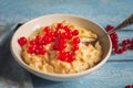 Breakfast of milk oatmeal with red currants in a deep white plate on a wooden tray, a spoon and a denim napkin, as well as sprigs