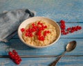 Breakfast of oatmeal with red currants on a blue wooden tray, spoon and denim napkin, as well as sprigs of currant, taken from the