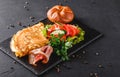 Breakfast, Omelette with bun, bacon, prosciutto, fresh salad and spices on stone board on black table surface.