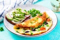 Omelette with tomatoes, black olives and sandwich with avocado on white plate.