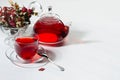 Breakfast with organic red hawthorn tea in transparent teapot, cup,  hawthorn berries, rose hip in sunlight with shadow on white. Royalty Free Stock Photo