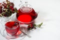 Breakfast with organic red hawthorn tea in transparent teapot, cup,  hawthorn berries, rose hip in sunlight with shadow on white. Royalty Free Stock Photo