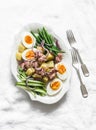 Breakfast plate - boiled eggs, potatoes, string beans, red onion, cucumber, canned tuna salad on a light background, top view