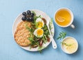 Breakfast plate - cracker, arugula, cherry tomatoes, boiled egg salad and green tea with lemon on blue background