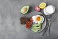 Breakfast plate, scrambled eggs on bread, avocado slices, tomato, whole grain bread, glass of milk, fork knife on a gray Royalty Free Stock Photo