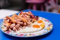 Breakfast, sausages, fried eggs and bacon wrapped cheese in the same plate, laying on a blue table