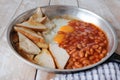 Breakfast served on frying pan consist of toast bread, bean and egg.