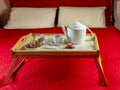 A breakfast is served on a wooden tray with folding legs on a red bed Royalty Free Stock Photo