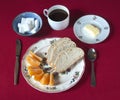 Breakfast set with coffee, bread, butter and orange wedges on a red tablecloth