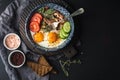 Breakfast set. Pan of fried eggs with bacon, fresh tomato, cucumber, sage and bread on dark serving board over black Royalty Free Stock Photo