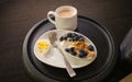 A breakfast snack of an hardboiled egg, yogurt, blueberries and cappuccino at an airport lounge