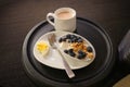 A breakfast snack of an hardboiled egg, yogurt, blueberries and cappuccino at an airport lounge