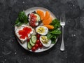 Breakfast, snack, tapas plate - sandwiches with red caviar, salmon, cream cheese, vegetables, spinach, boiled egg on a dark Royalty Free Stock Photo