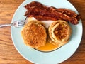 Breakfast of stacks of pancakes, syrup, bacon strips, on a plate with a fork.