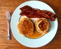 Breakfast of stacks of pancakes, syrup, bacon strips, on a plate with a fork.