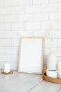 Breakfast still life. Picture frame mockup, tray of hot drink, vase of dried flowers, candles. Brick tiles wall on background.