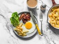 Breakfast table - fried egg, bacon, green salad, hash potatoes and coffee with cream on a light marble background, top view Royalty Free Stock Photo