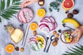 Breakfast table with yogurt acai bowls and fresh tropic fruits on a gray stone background with wooman hand and palm