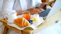 Breakfast in a tray on the bed in the luxury hotel room in front of an Asian businesswoman traveler using a laptop Royalty Free Stock Photo