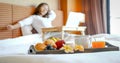 Breakfast in a tray on the bed in the luxury hotel room in front of an Asian woman traveler using a laptop Royalty Free Stock Photo