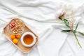 Breakfast on the tray with granola, tea and fruit on white bed sheet background top view