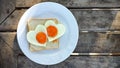 Breakfast for Valentines day with love. Fried eggs in the shape of a heart at toast on white plate and wooden table on the beach Royalty Free Stock Photo