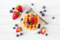 Breakfast waffles with strawberries and blueberries. Top view over white wood.