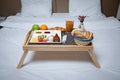 Breakfast on a white plate on a wooden tray with legs lying on a white blanket and bed.Isolated on bed background and two white pi