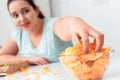 Breaking Diet. Chubby girl sitting at kitchen table eating chips excited close-up blurred background