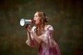 One adorable blond princess wearing fancy pink dress shouting through megaphone over vintage texture background