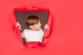 Breaking paper background. Kid shows face in paper hole. Positive child with on face, keeps through torn hole in red Royalty Free Stock Photo