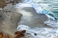 Breaking tourqoise wave on dark sandy beack with foam trails and rocks Royalty Free Stock Photo