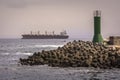 Breakwater made with concrete cubes and a green tower with a little boat and a big ship in the sea. Antofagasta, Chile