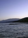 Breakwater on the shore of a calm sea against the background of coastal mountains in the haze of the sky in the distance in the