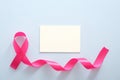 Breast cancer awareness month concept. Empty paper card mockup and pink breast cancer ribbon on blue background Royalty Free Stock Photo