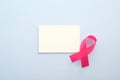 Breast cancer awareness month concept. Empty paper card mockup and pink breast cancer ribbon on blue background Royalty Free Stock Photo