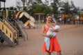 Breast feeding: Young mother breastfeeds her baby boy child in city park standing wearing bright red dress - Son wears Royalty Free Stock Photo