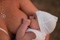 Breast feeding: Young mother breastfeeds her baby boy child outdoors wearing bright red dress - Son wears white cap - Royalty Free Stock Photo