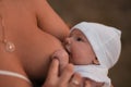 Breast feeding: Young mother breastfeeds her baby boy child outdoors wearing bright red dress - Son wears white cap - Royalty Free Stock Photo